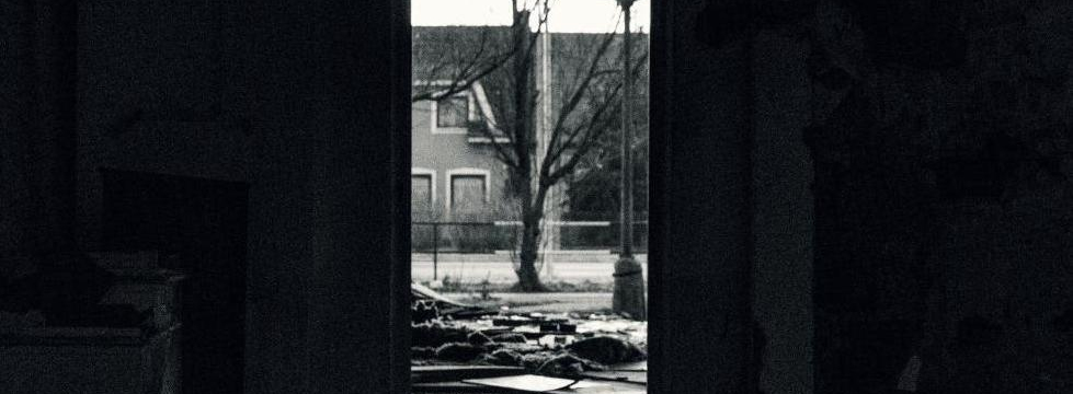 Durch einen Türrahmen blickt aus einem zertümmerten Wohnbereich auf Straße mit einem Baum in der Mitte